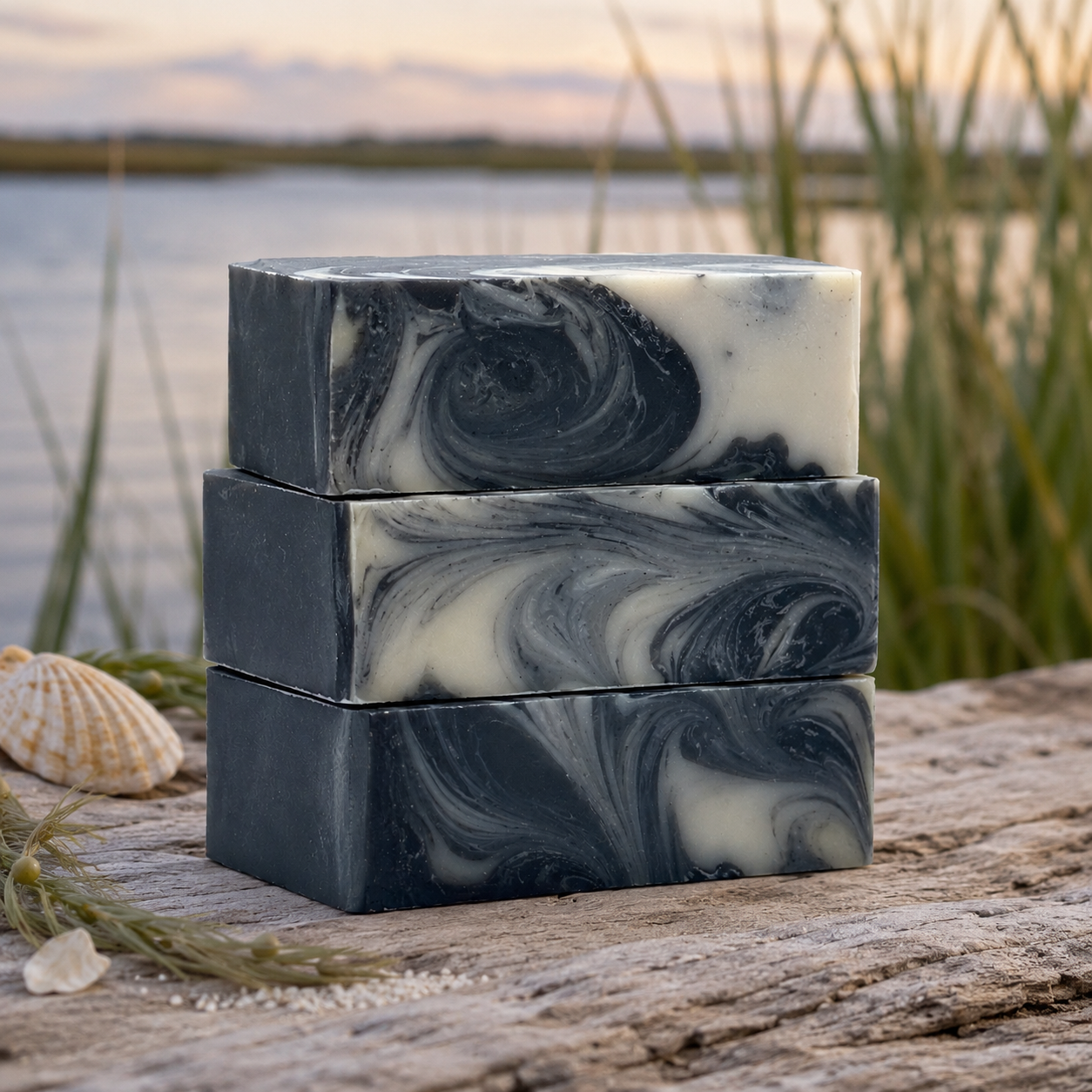 Moonlit Marsh Cleansing Bar - stacked handcrafted charcoal soap bars with black and white swirls on driftwood by a marsh